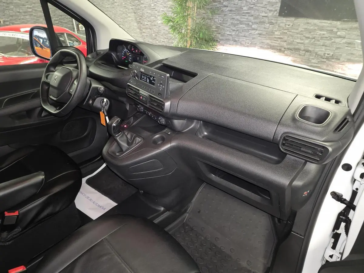 Intérieur avant droit du Peugeot Partner 2021, tableau de bord noir avec volant, levier de vitesse manuel et sièges en cuir noir.