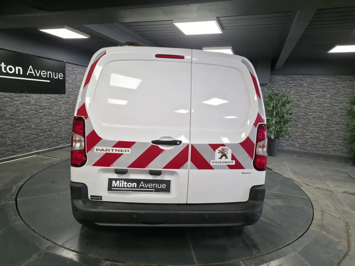 Vue arrière d'un Peugeot Partner blanc avec bandes réfléchissantes rouges et blanches et portes battantes tôlées.