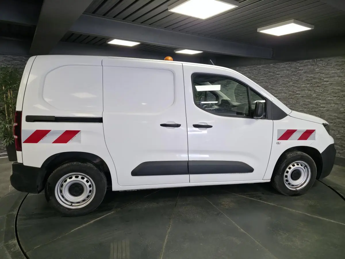Vue latérale droite d’un Peugeot Partner blanc avec bandes réfléchissantes rouges et éléments noirs sur les portes.
