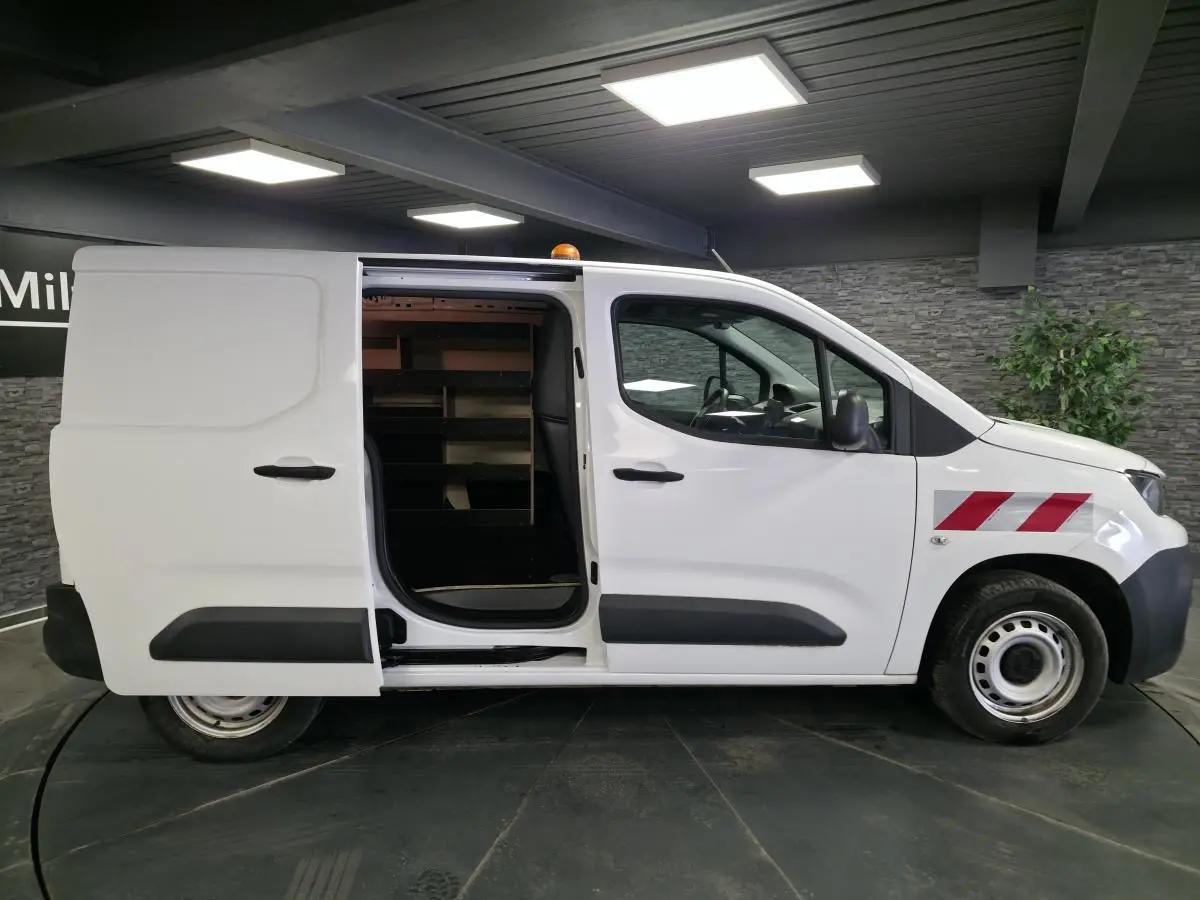 Vue latérale droite d’un Peugeot Partner blanc avec porte coulissante ouverte et bandes rouges diagonales sur l’aile avant.
