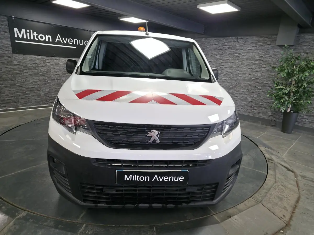 Vue avant d'un Peugeot Partner blanc avec bandes rouges diagonales sur le capot, en intérieur showroom.