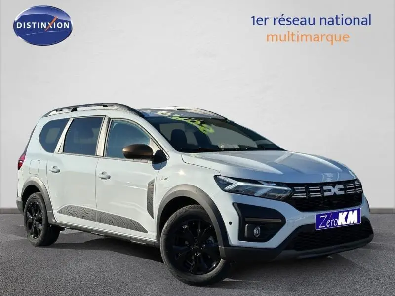 Dacia Jogger blanc glacier en 3/4 avant droit avec jantes noires et barres de toit visibles.