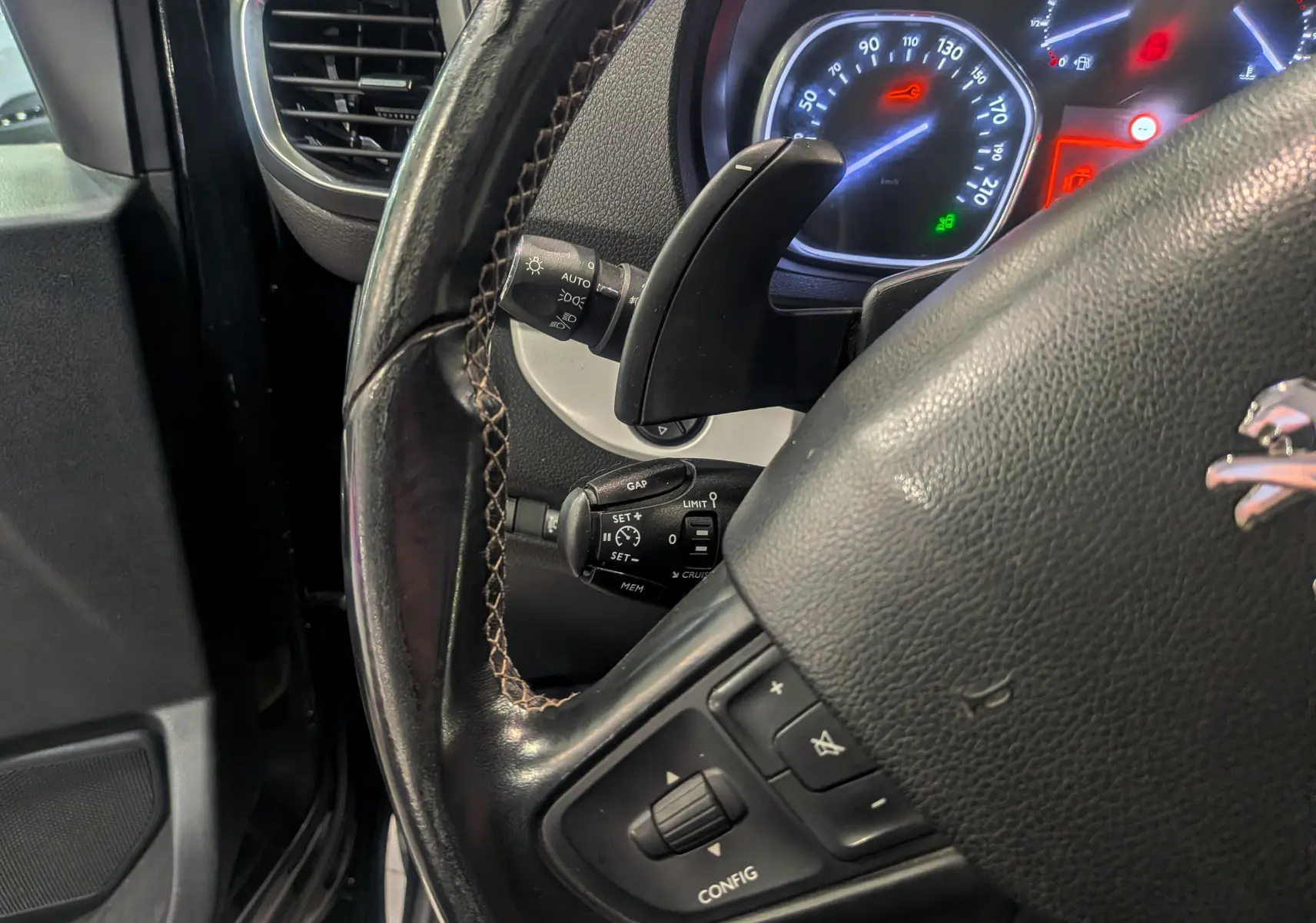 Gros plan sur le volant noir en cuir du Peugeot Expert Fourgon, avec commandes intégrées et tableau de bord éclairé en arrière-plan.