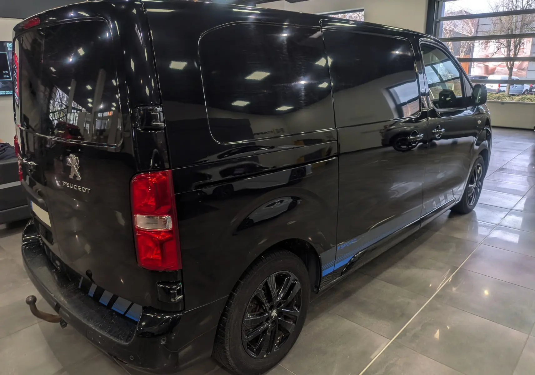 Vue 3/4 arrière droite du Peugeot Expert Fourgon noir Perla avec jantes noires et bande bleue Sport sur le bas de caisse.
