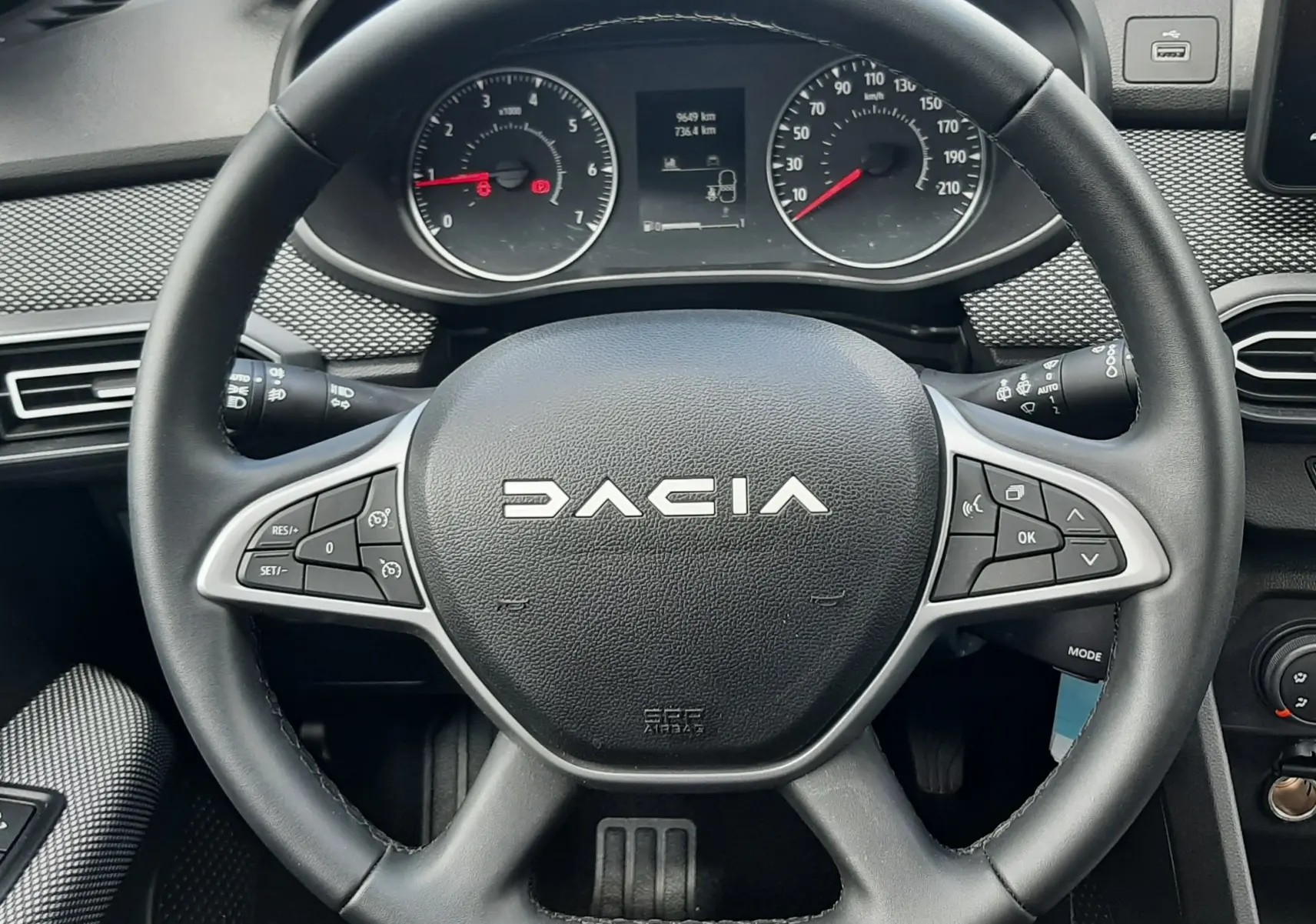 Vue rapprochée du volant noir multifonction d'une Dacia Sandero 2024, avec tableau de bord et compteur visible.