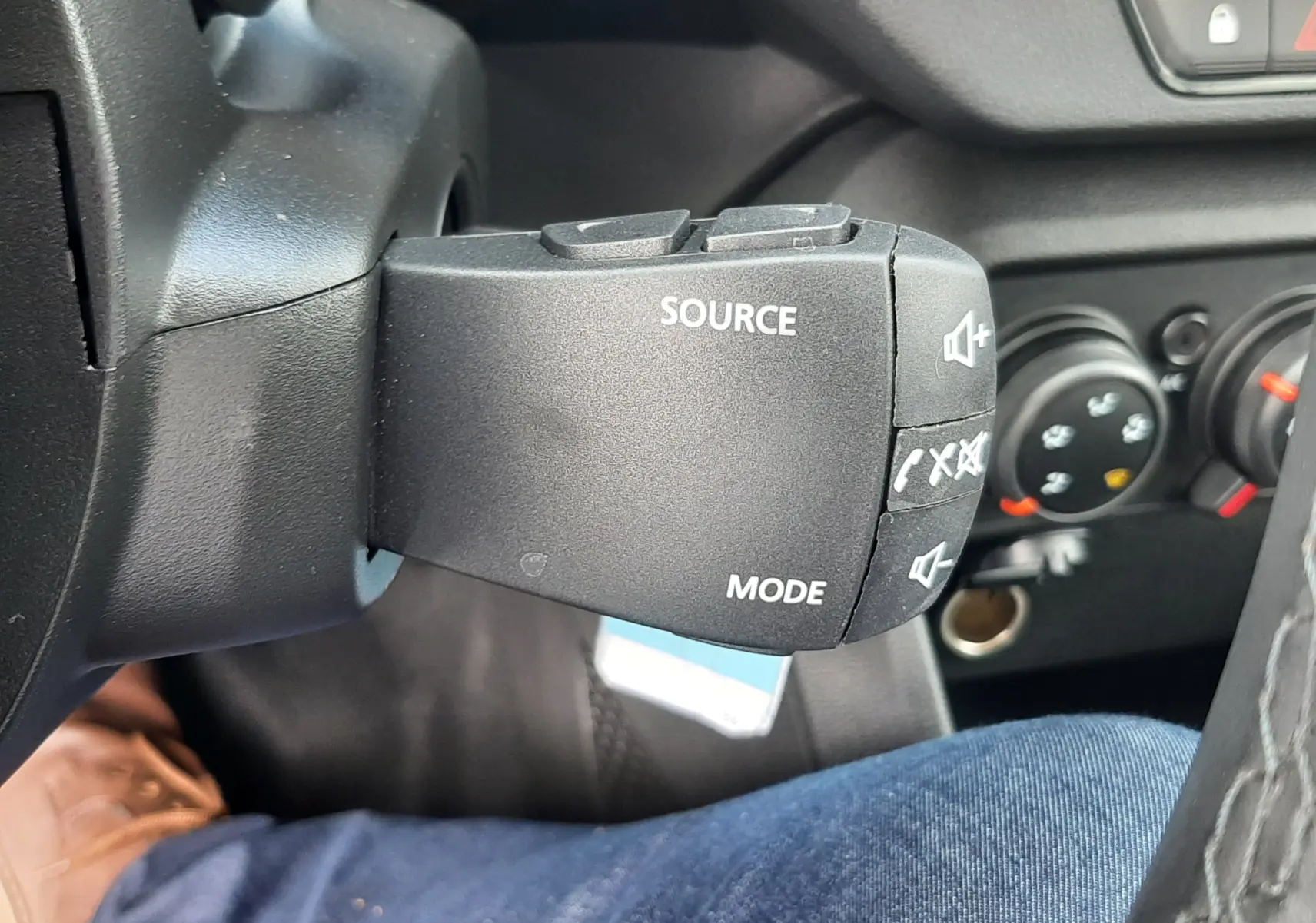 Gros plan sur la commande au volant noire du DACIA Sandero 2024, avec boutons source et mode visibles côté gauche.