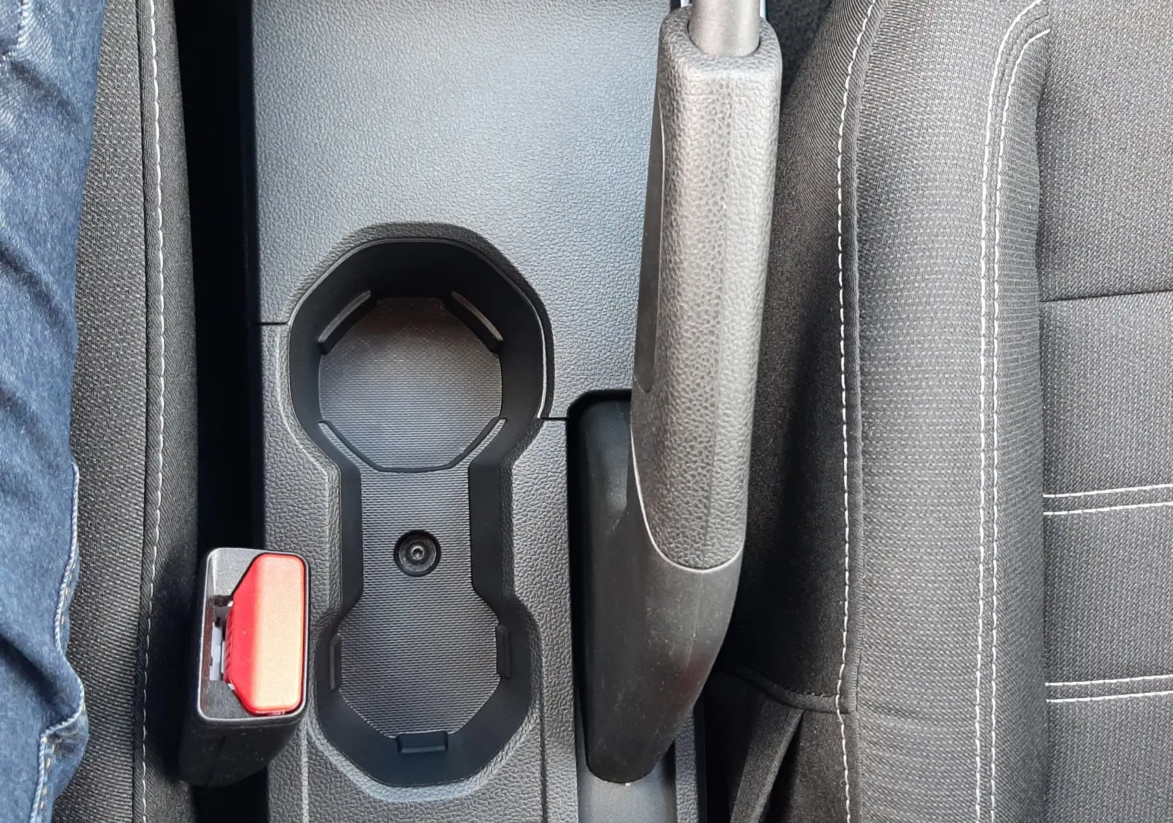 Vue plongeante sur la console centrale noire du Dacia Sandero 2024, avec frein à main, porte-gobelets et ceintures rouges.