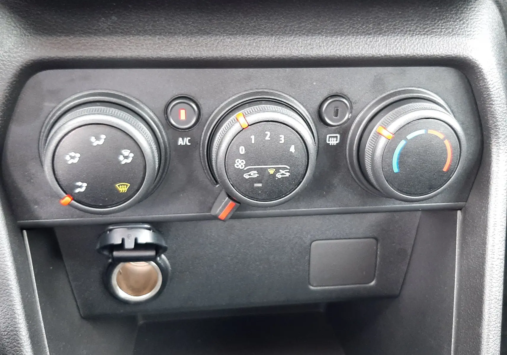 Vue rapprochée des commandes de climatisation manuelle noires du tableau de bord de la Dacia Sandero blanc glacier 2024.
