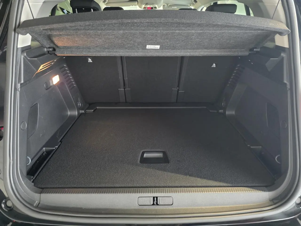 Coffre ouvert vu de l'arrière d'un Citroën C5 Aircross noir métallisé avec cache-bagages relevé.