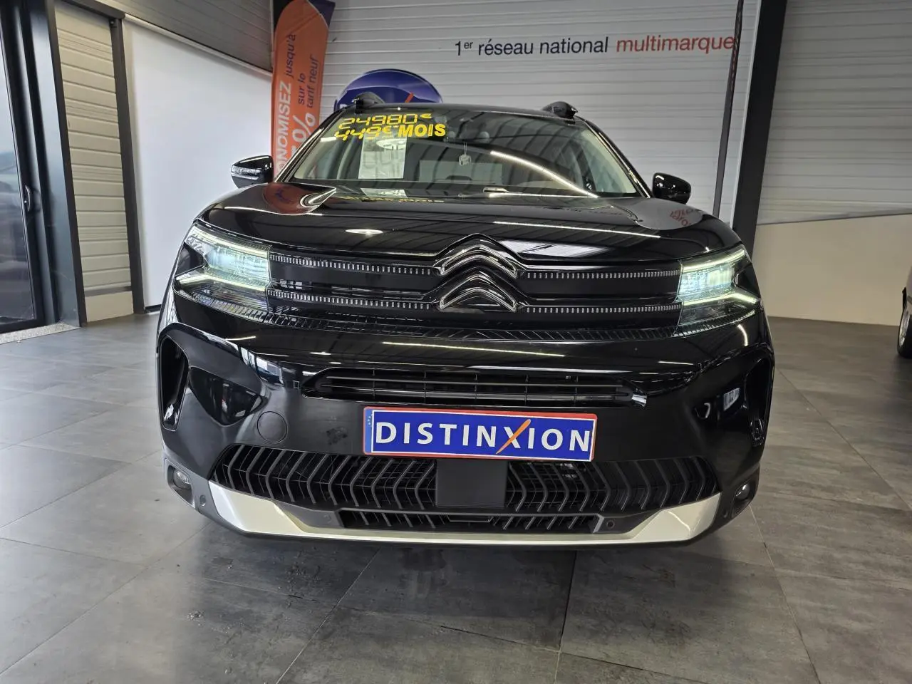 Vue avant d'un Citroën C5 Aircross noir métal avec calandre noire brillante et plaque Distinxion en intérieur showroom.