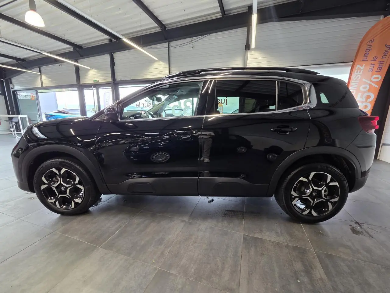 Vue latérale droite d'un Citroën C5 Aircross noir métallisé avec jantes alliage bi-ton en showroom.