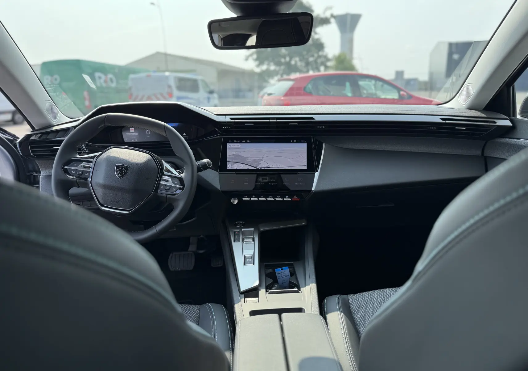 Intérieur moderne de la Peugeot 308 2025 en gris, vue depuis l'arrière montrant le volant compact et l'écran tactile central.