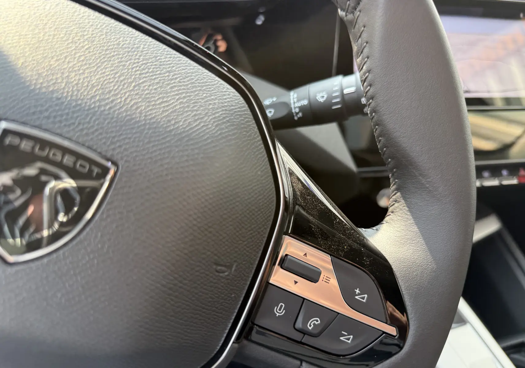 Gros plan sur le volant cuir noir de la Peugeot 308 2025 avec commandes intégrées et logo visible.