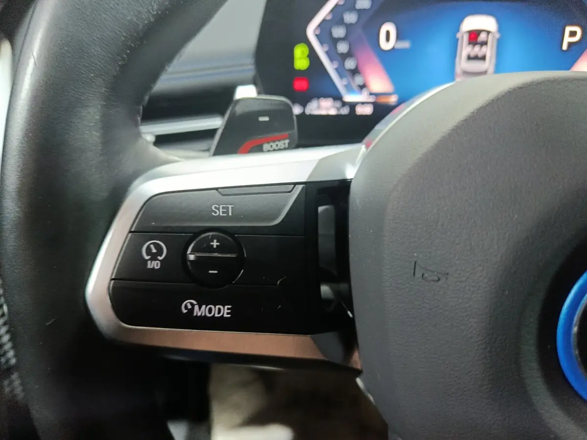 Gros plan sur les commandes du volant cuir noir du BMW X1 xDrive25e blanc, avec affichage numérique en arrière-plan.