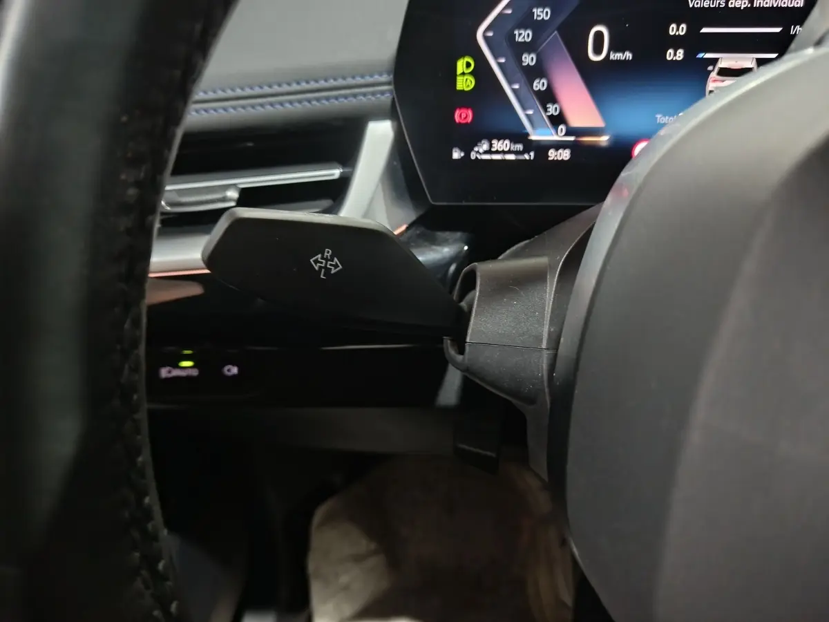 Gros plan sur le combiné d'instruments digital et levier de clignotant dans l'habitacle noir du BMW X1 hybride 2024.