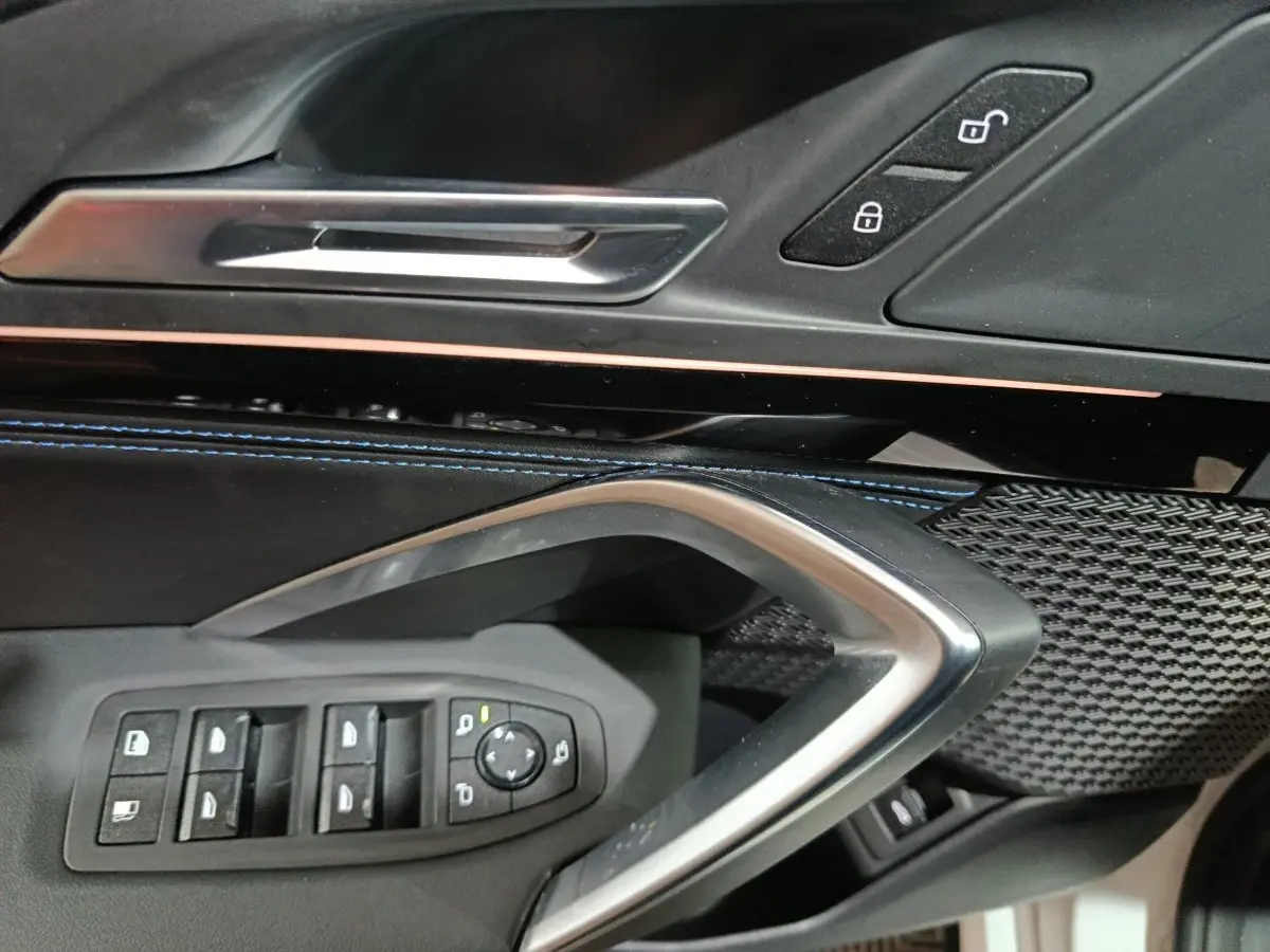 Détail intérieur côté conducteur BMW X1 xDrive25e blanc 2024, commandes vitres et poignée argentée.