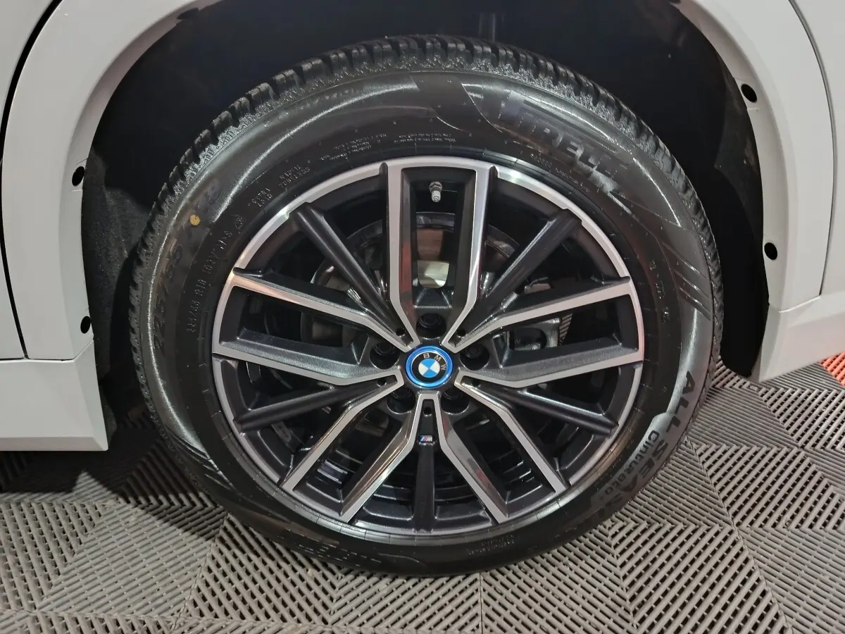 Gros plan sur la jante noire et argentée avec logo BMW d'un BMW X1 blanc, roue avant gauche visible.