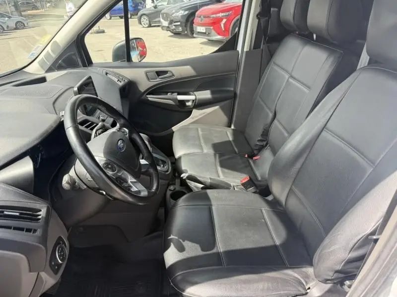 Vue intérieure côté conducteur du Ford Transit Connect blanc glacier de 2019, sièges en cuir noir et volant multifonction.