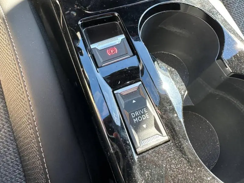 Gros plan sur la console centrale noire brillante du Peugeot 2008 Hybrid 2025, montrant le bouton Drive Mode et frein à main électrique.