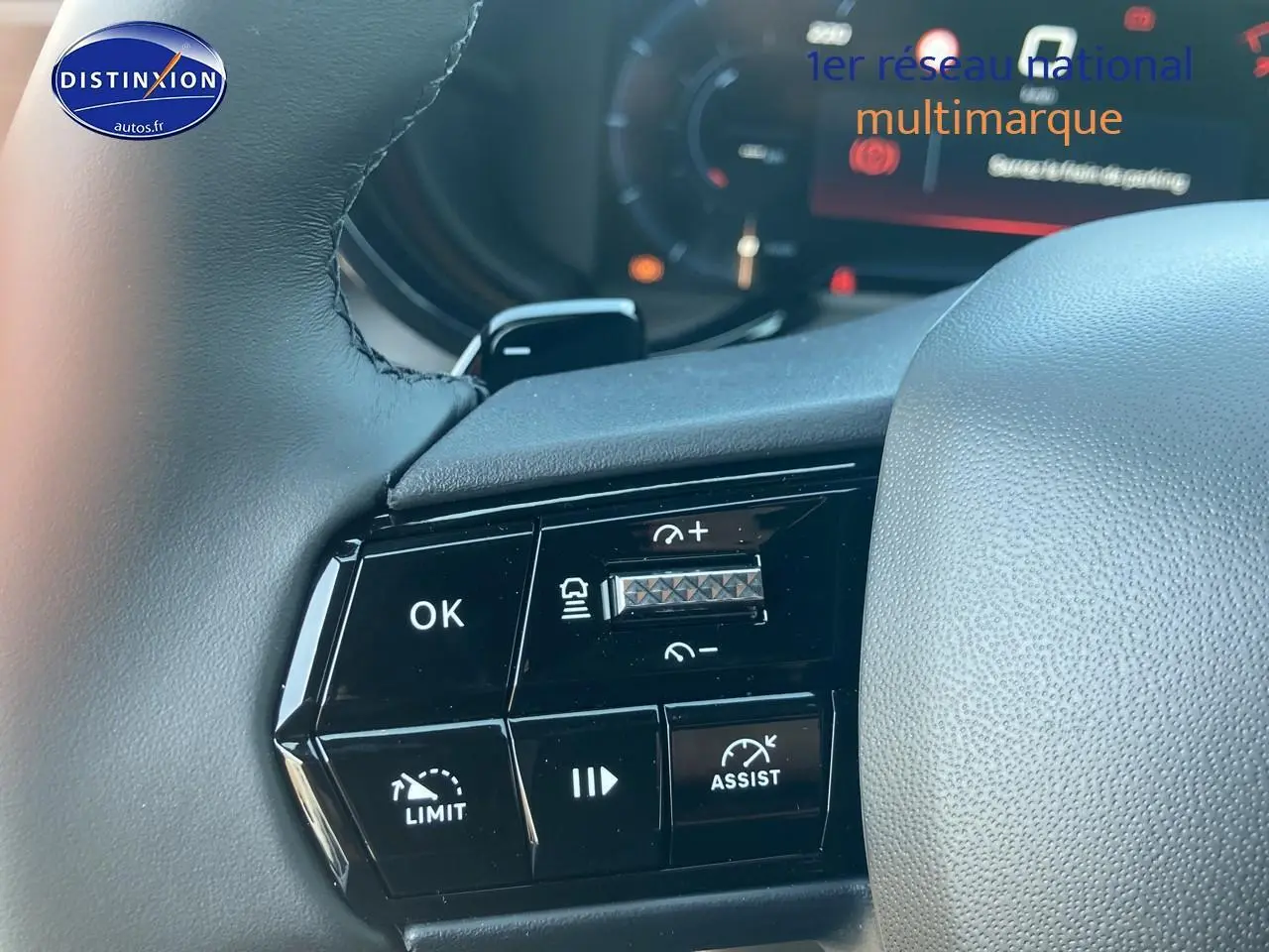 Gros plan sur les commandes à gauche du volant gris d'une Alfa Romeo Junior 1.2 hybride 2026, boutons noirs avec marquages blancs.