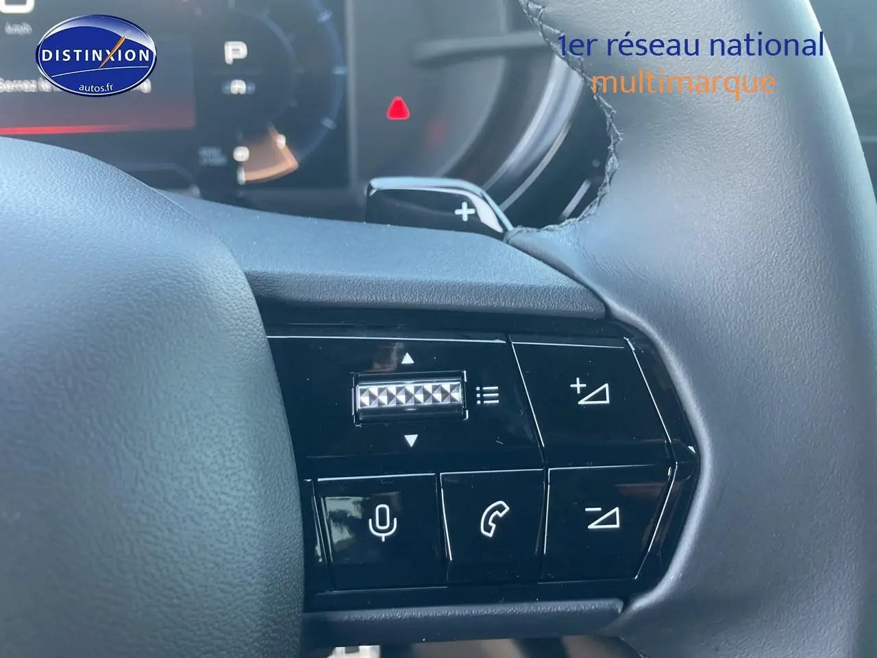 Gros plan sur les commandes au volant à gauche de l'Alfa Romeo Junior ivoire et noir, avec boutons de volume et téléphone visibles.