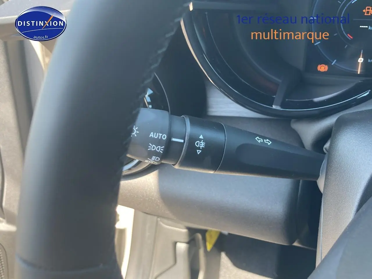 Gros plan sur le commodo d’éclairage et clignotants derrière le volant d’une Alfa Romeo Junior ivoire et noir.