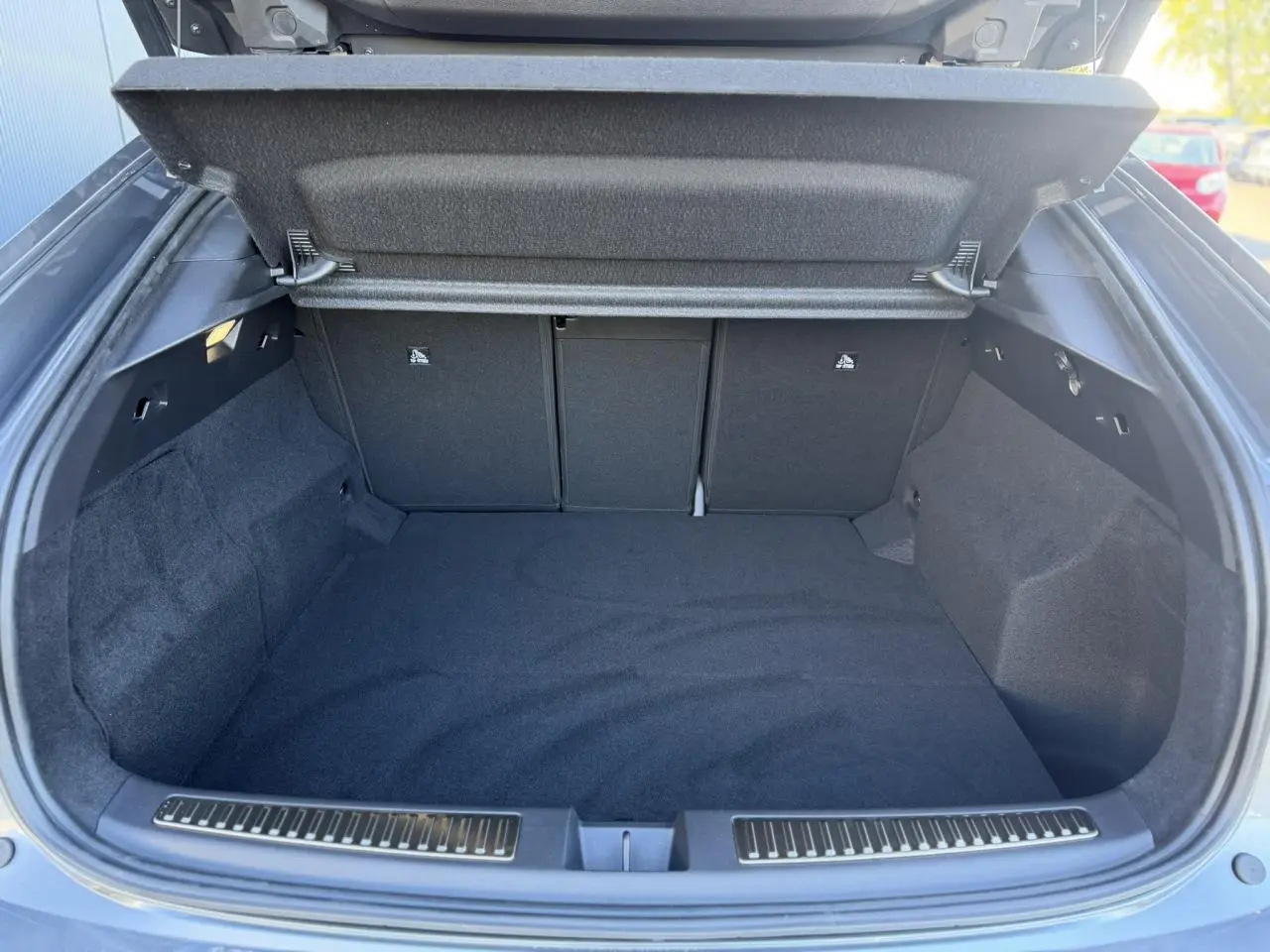 Coffre ouvert vu de l'arrière d'une Renault Rafale gris schiste avec hayon électrique, espace de chargement vide et tapis noir.