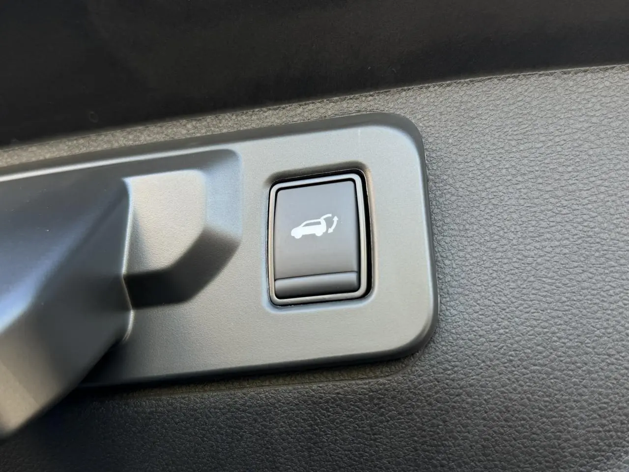 Bouton d'ouverture électrique du hayon sur panneau intérieur noir du Renault Rafale E-Tech Gris Schiste.