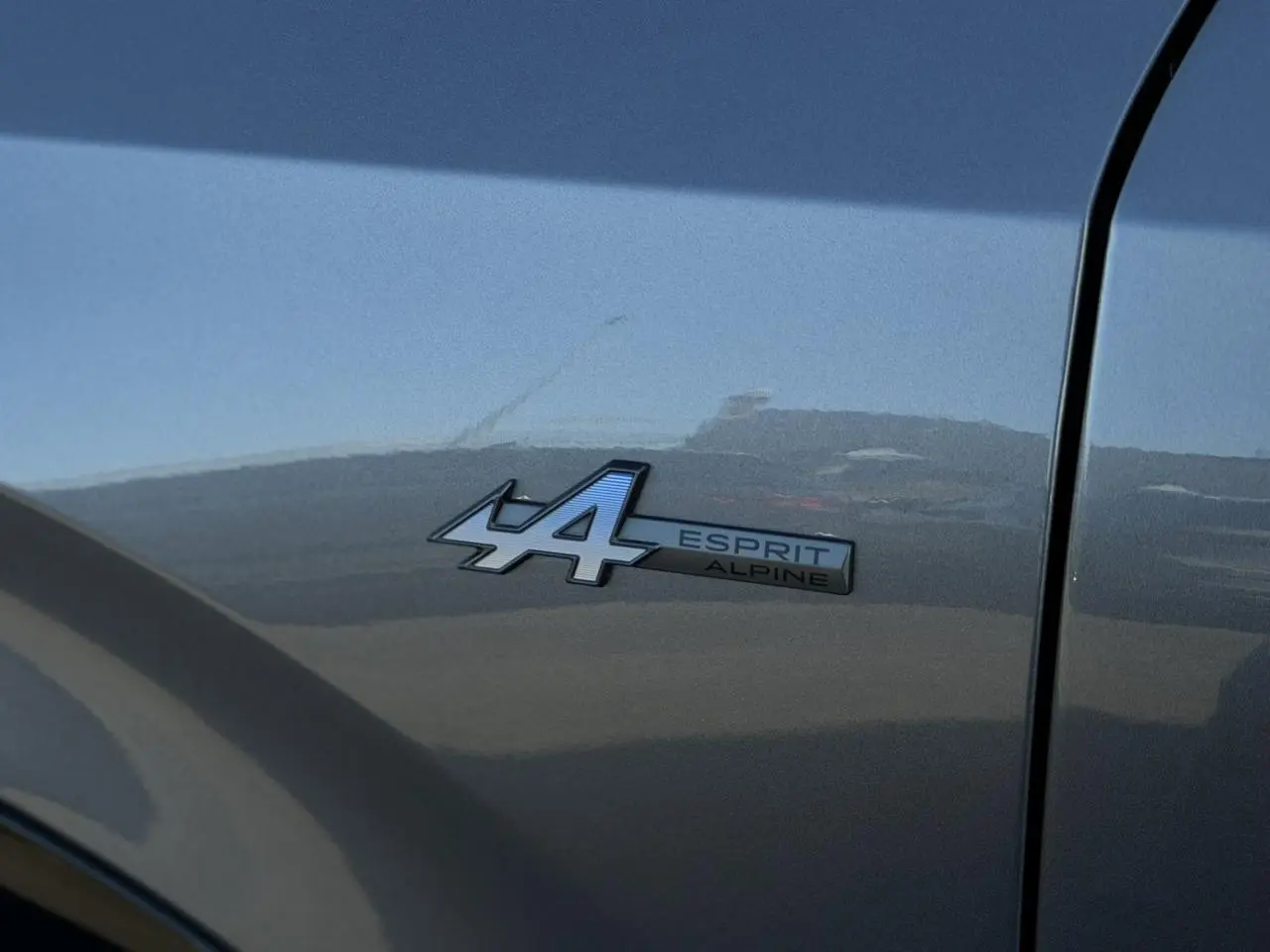 Gros plan sur le badge Esprit Alpine bleu sur la porte avant droite d’un Renault Rafale gris schiste.