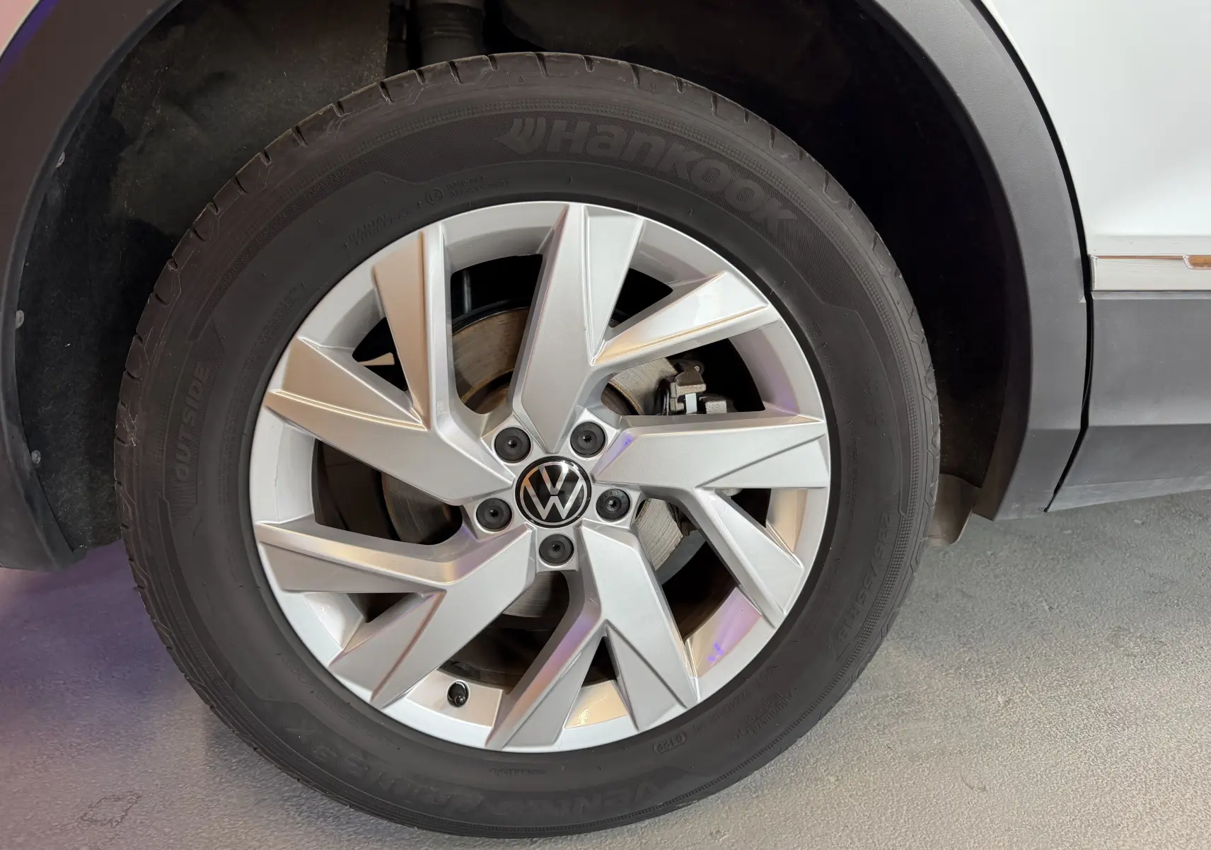 Gros plan sur la roue avant gauche gris clair du Volkswagen Tiguan 1.4 E-HYBRID 2022 avec jante alliage et logo VW au centre.