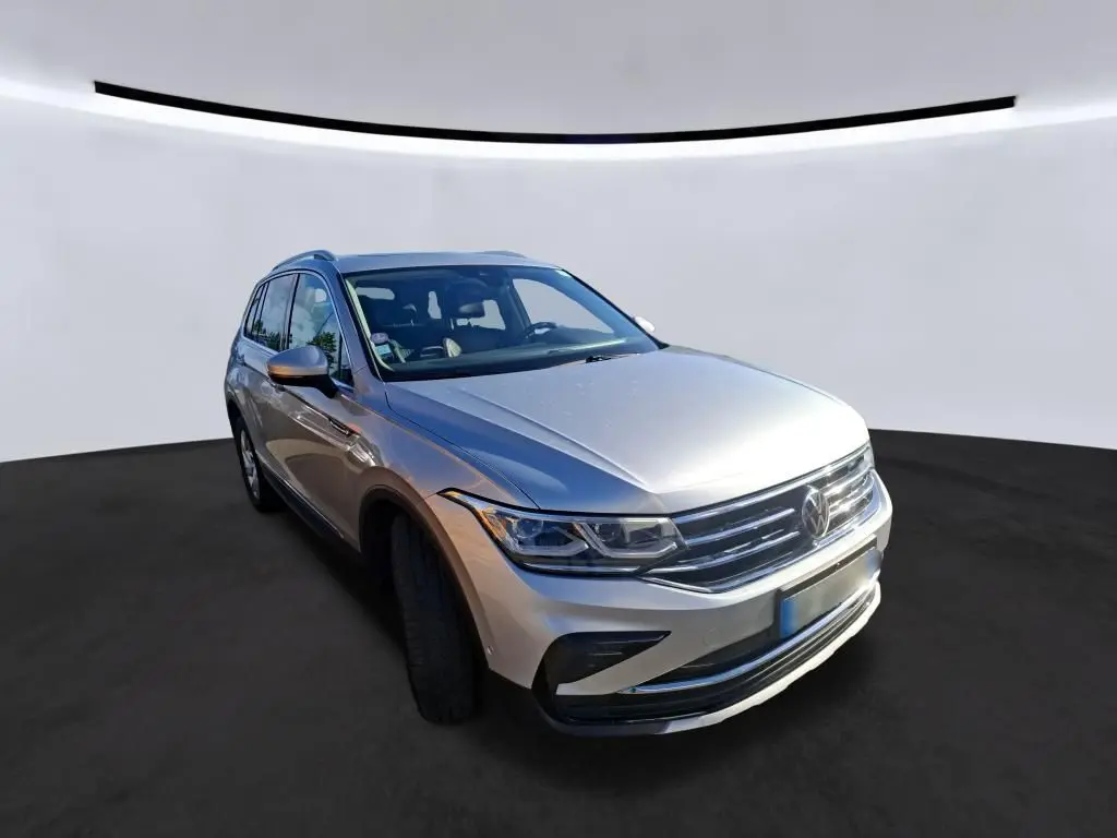 Volkswagen Tiguan gris clair en 3/4 avant droit, mettant en valeur sa calandre chromée et ses phares LED distinctifs.