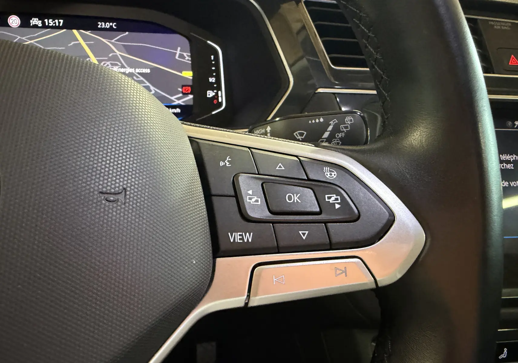 Gros plan sur le volant noir du Volkswagen Tiguan 1.4 E-HYBRID 2022, avec commandes multifonctions et tableau de bord numérique en arrière-plan.