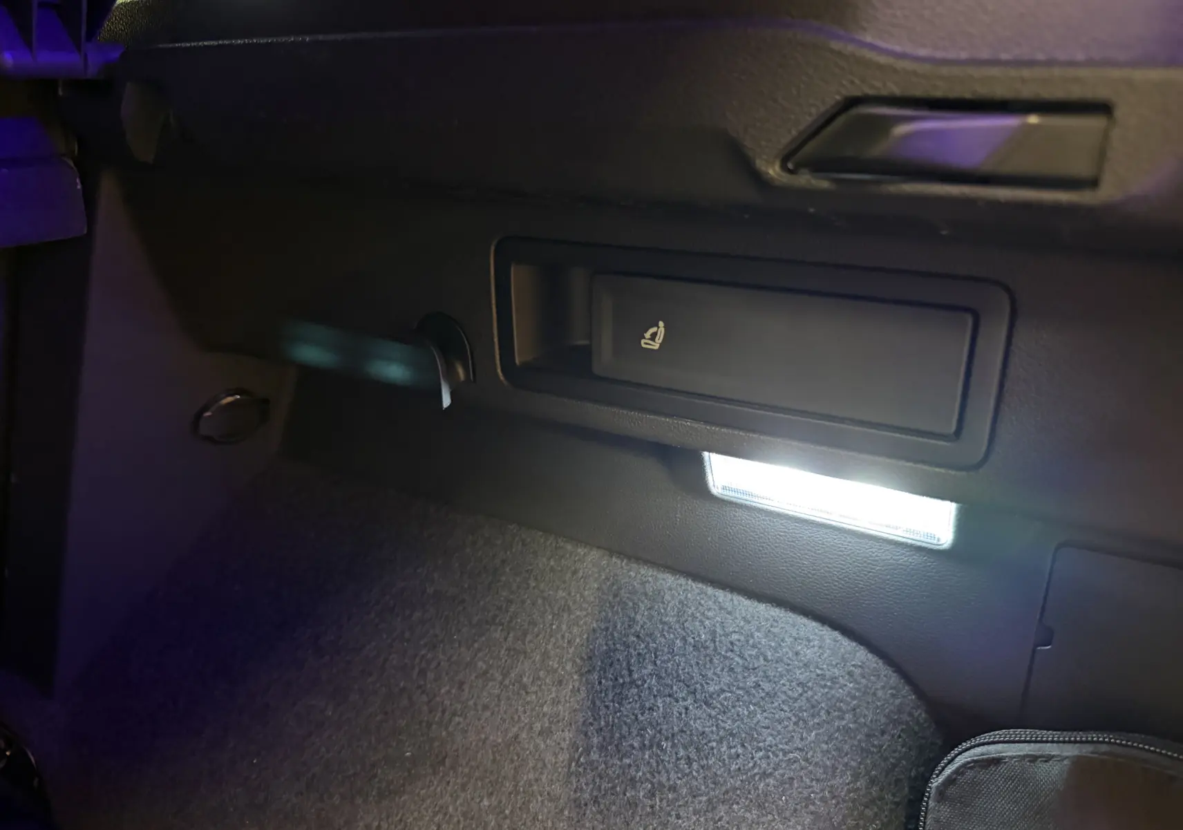 Détail intérieur du coffre du Volkswagen Tiguan 2022 gris clair, montrant le levier de rabattement des sièges et un éclairage LED.