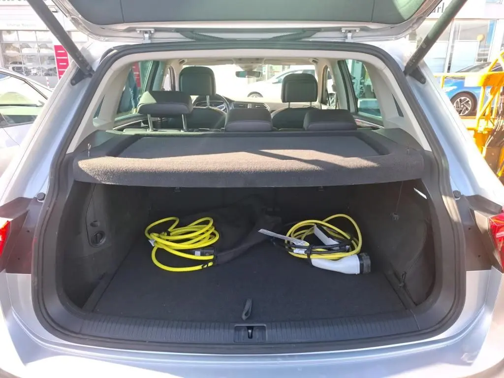 Vue arrière du coffre ouvert d'un Volkswagen Tiguan gris clair 2022, avec câbles de recharge hybride visibles à l'intérieur.