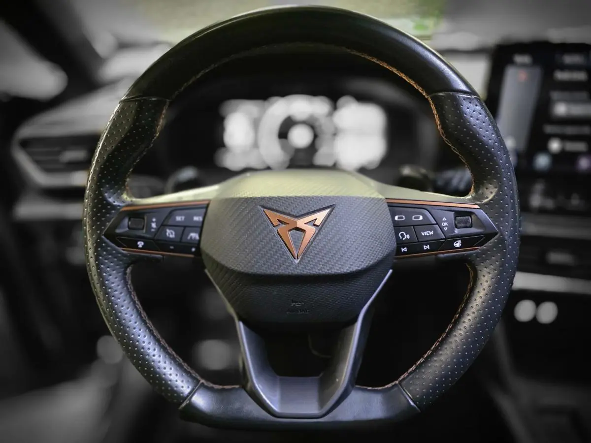 Volant sport noir perforé avec surpiqûres cuivre et logo CUPRA en cuivre au centre, vue frontale rapprochée.
