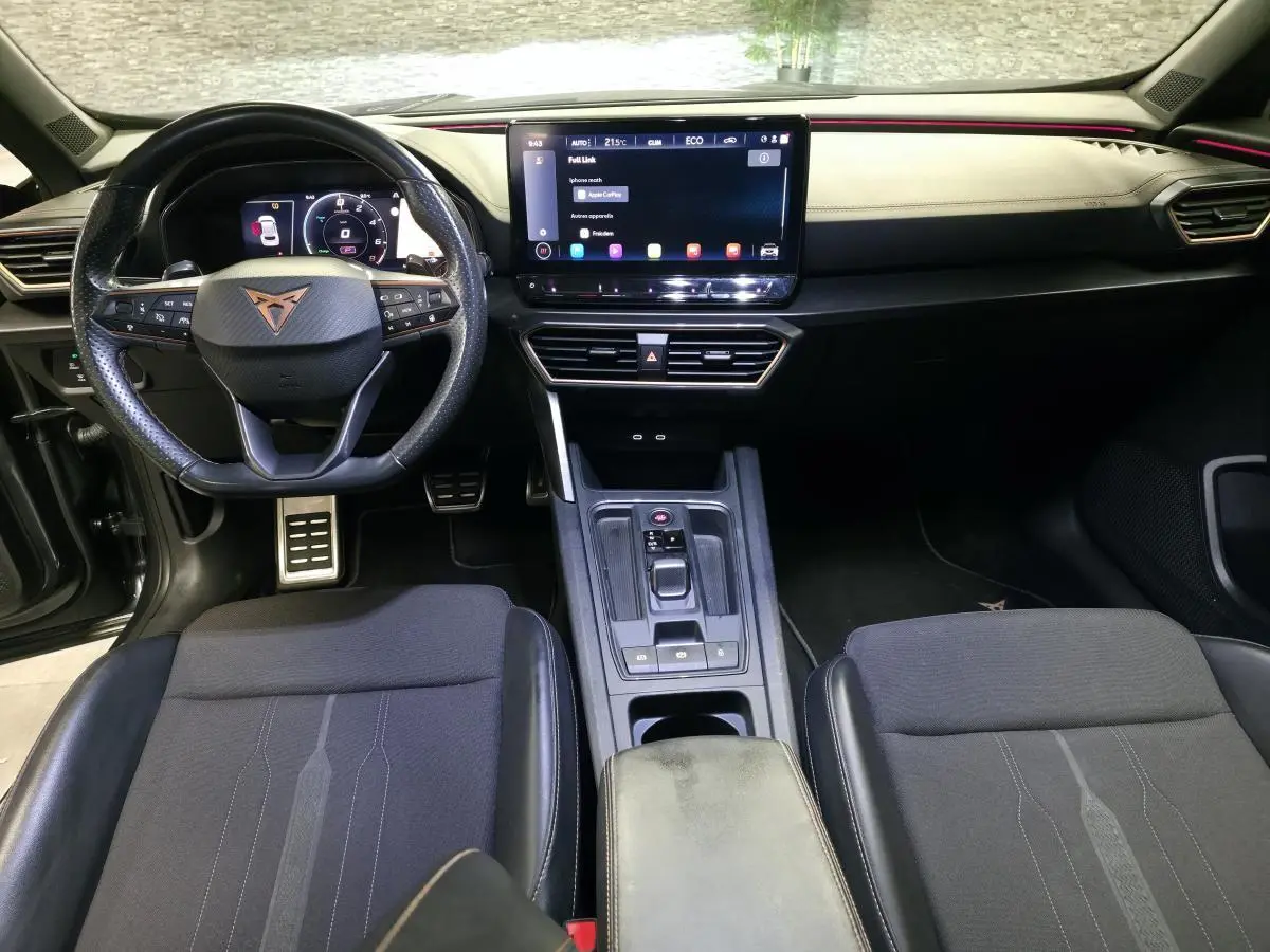 Vue intérieure avant du CUPRA Formentor 1.4 e-Hybrid 2024, tableau de bord noir avec écran tactile et volant sport cuir.