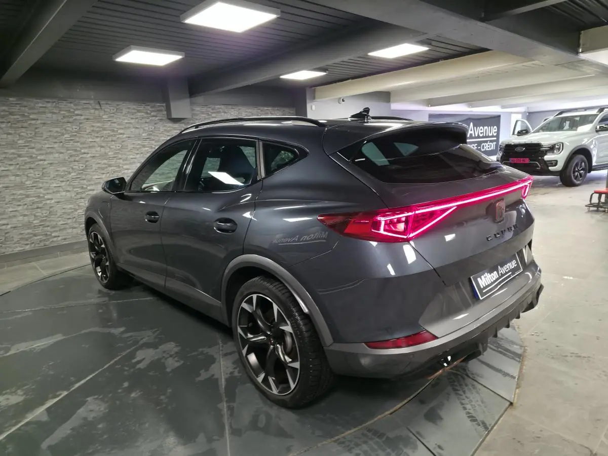 Vue 3/4 arrière droite du CUPRA Formentor gris avec bandeau LED arrière et jantes alliage noires en intérieur showroom.