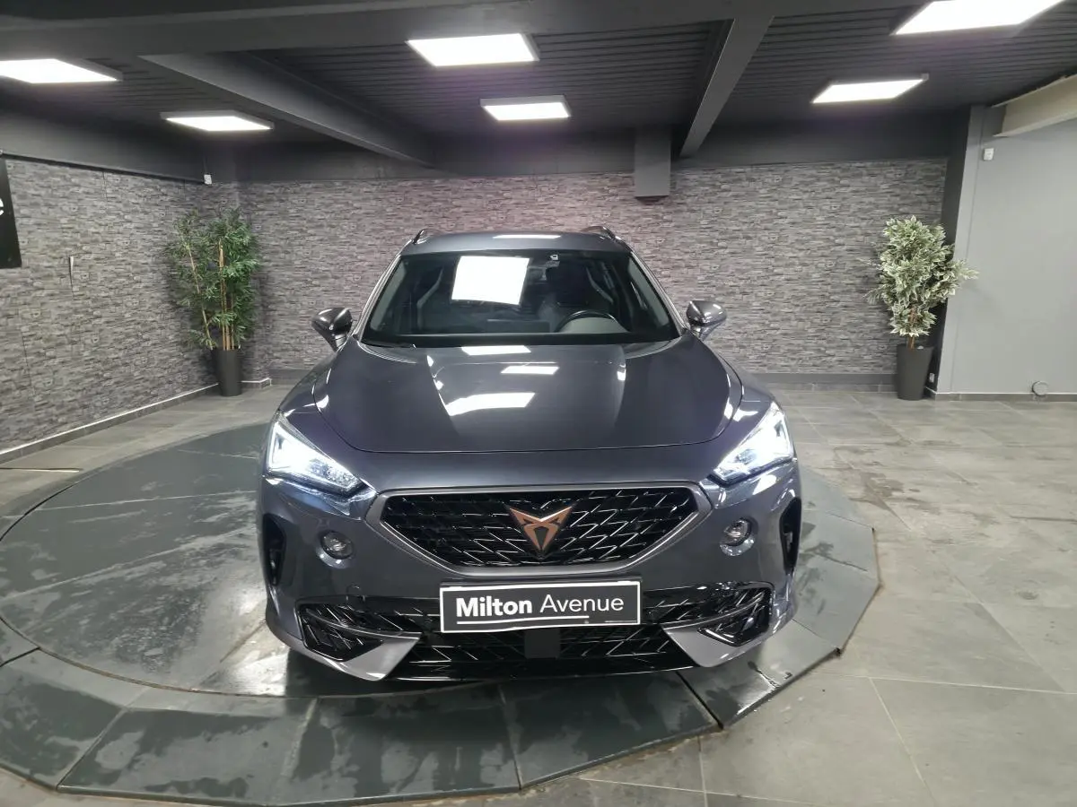 Vue avant d'un CUPRA Formentor gris avec calandre noire et logo cuivre, dans un showroom intérieur.