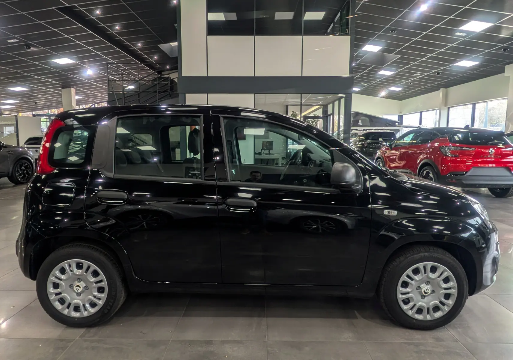 Profil côté gauche d'une Fiat Panda 1.0 70 CH Hybrid City noire, en intérieur de showroom lumineux.