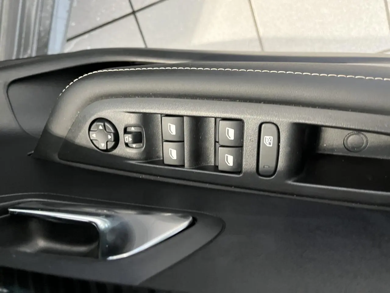 Détail des commandes des vitres et rétroviseurs sur la porte avant gauche d'une Peugeot 208 gris clair Selenium.