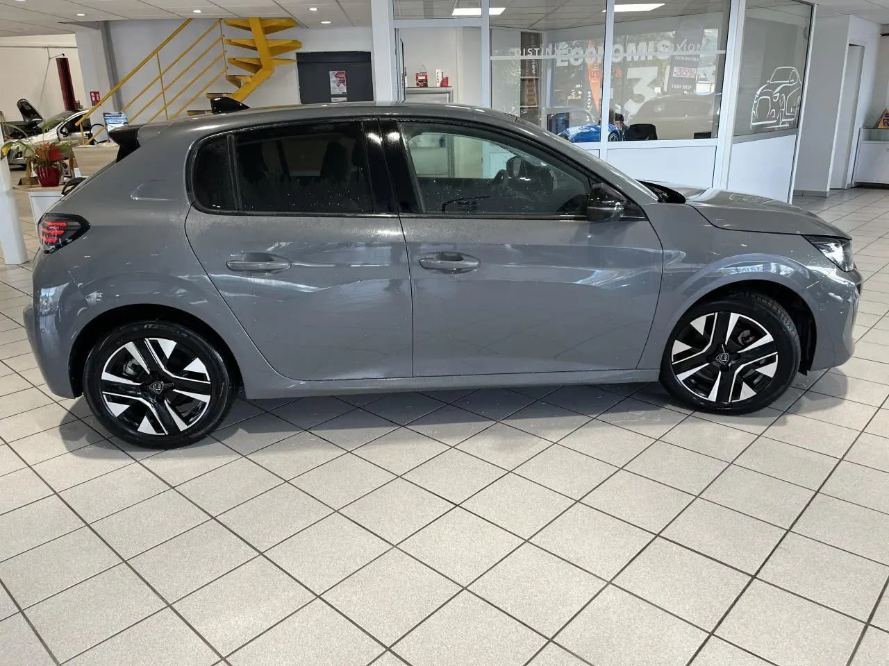 Peugeot 208 gris clair sélénium vue de profil côté gauche, avec jantes alliage bi-tons et vitres teintées.