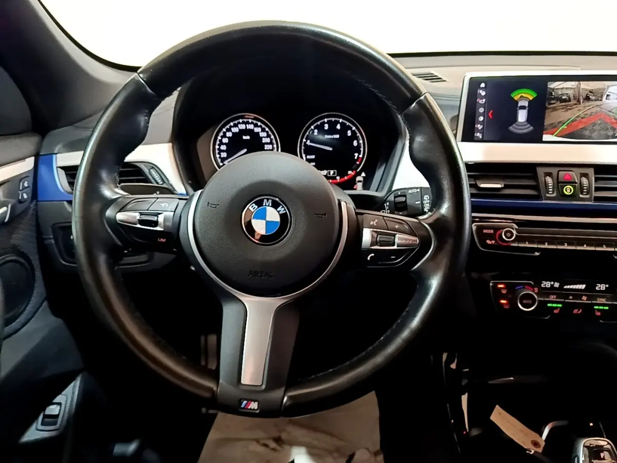 Vue intérieure centrée sur le volant cuir BMW M avec tableau de bord digital et écran tactile 8,8 pouces du BMW X1 blanc.