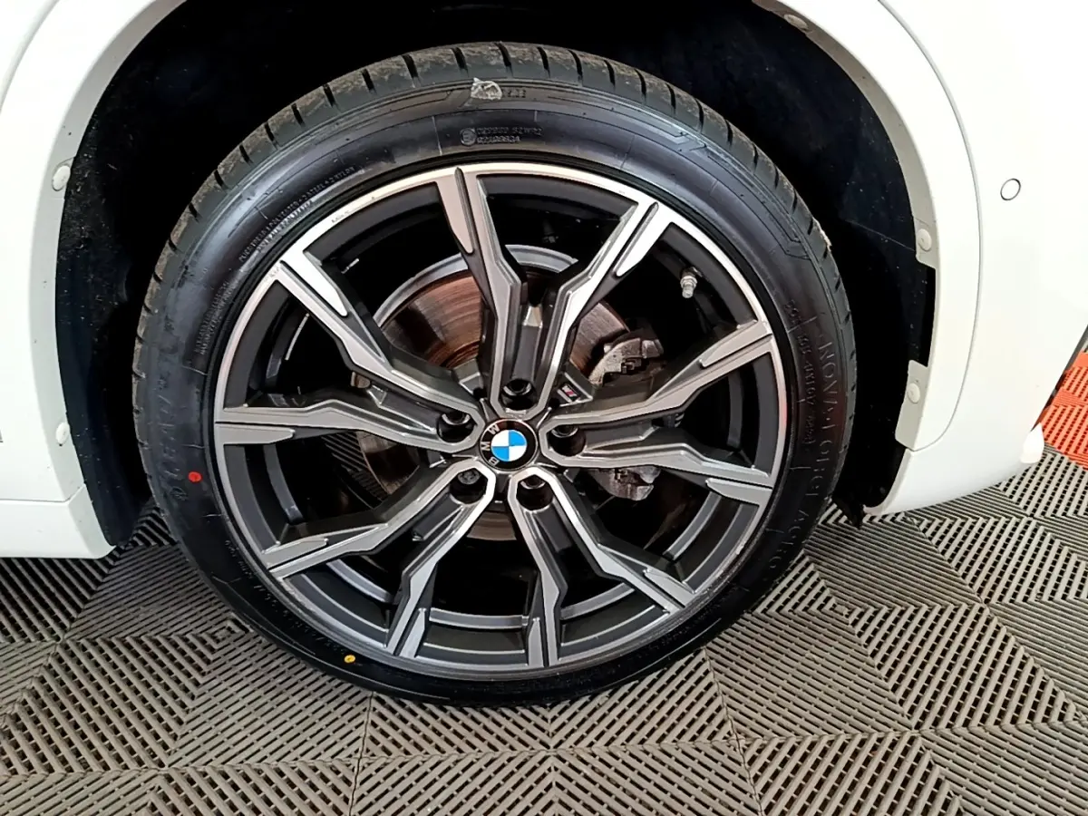 Gros plan sur la roue avant droite d'un BMW X1 blanc, avec jante alliage M Sport à design étoilé.