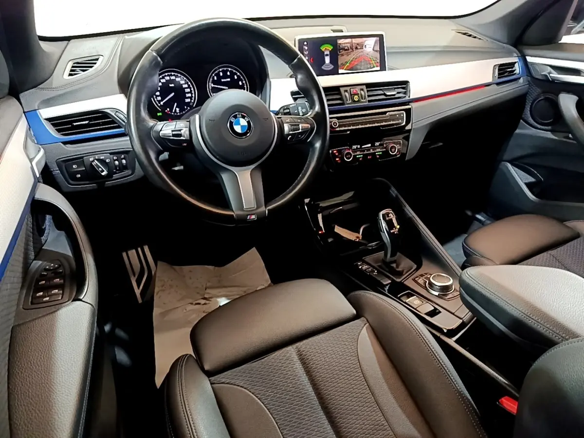 Vue intérieure avant droite du BMW X1 sDrive18i M Sport 2022, volant cuir, écran tactile et console centrale noire.