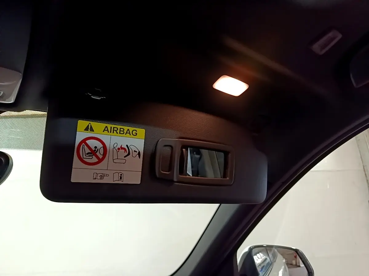Vue intérieure rapprochée du pare-soleil côté conducteur avec miroir et avertissement airbag dans un BMW X1 blanc.