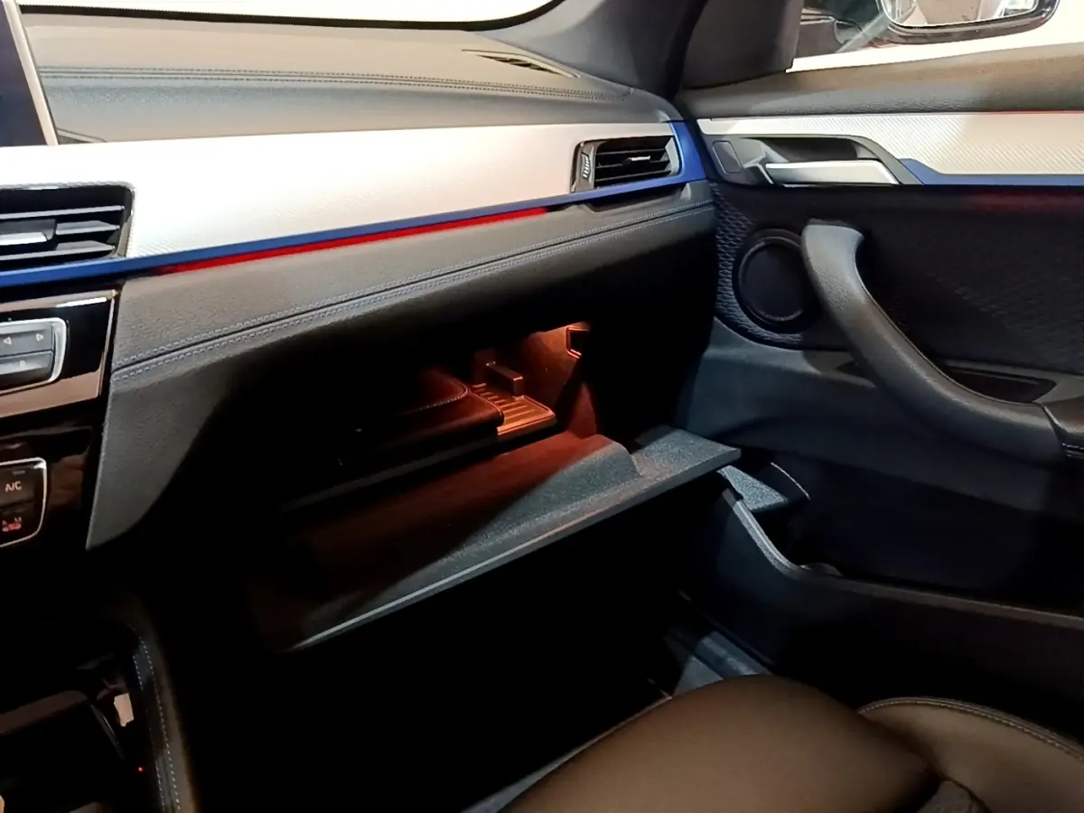 Intérieur côté passager du BMW X1 blanc 2022, vue sur boîte à gants ouverte et détails du tableau de bord noir et argent.