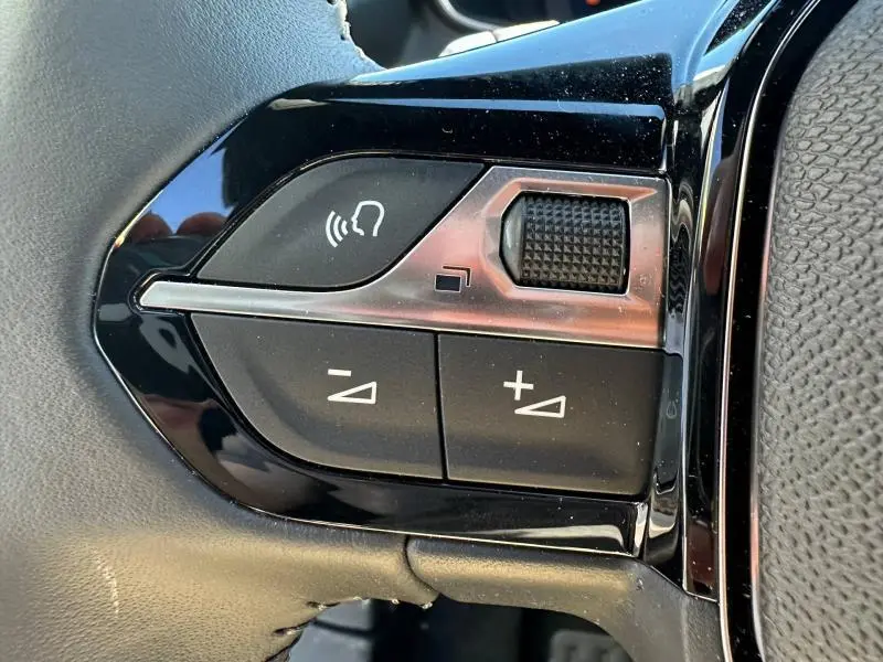 Gros plan sur les commandes de volume et de reconnaissance vocale sur le volant noir du Peugeot 2008 hybride 2025.