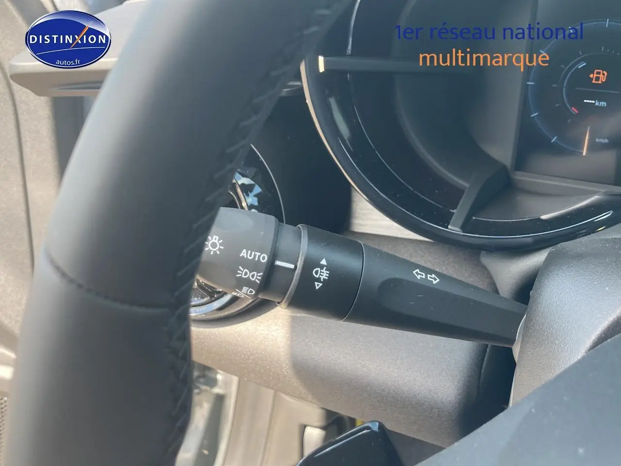 Gros plan sur la manette de clignotants et phares à gauche du volant d'une Alfa Romeo Junior grise, tableau de bord partiellement visible.
