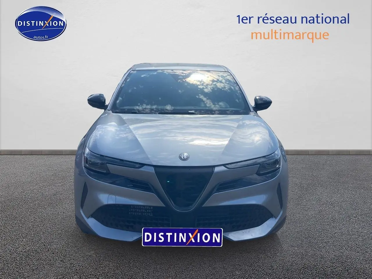 Vue frontale d'une Alfa Romeo Junior 1.2 hybride gris métallisé avec calandre triangulaire distinctive et phares fins.