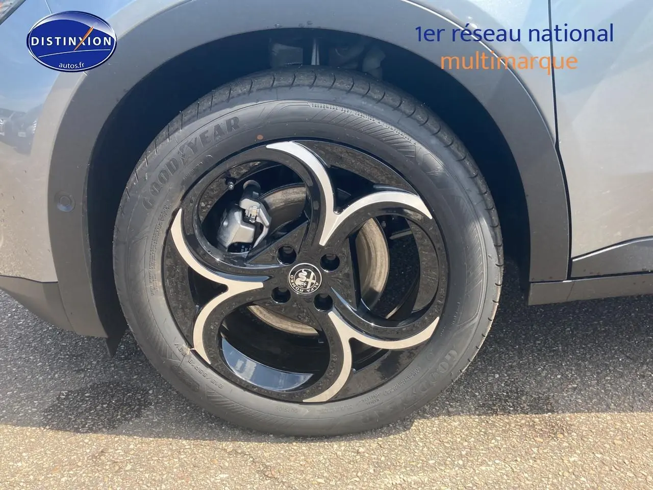 Gros plan sur la roue arrière gauche grise d'une Alfa Romeo Junior 1.2 hybride avec jante alliage noire et argent.